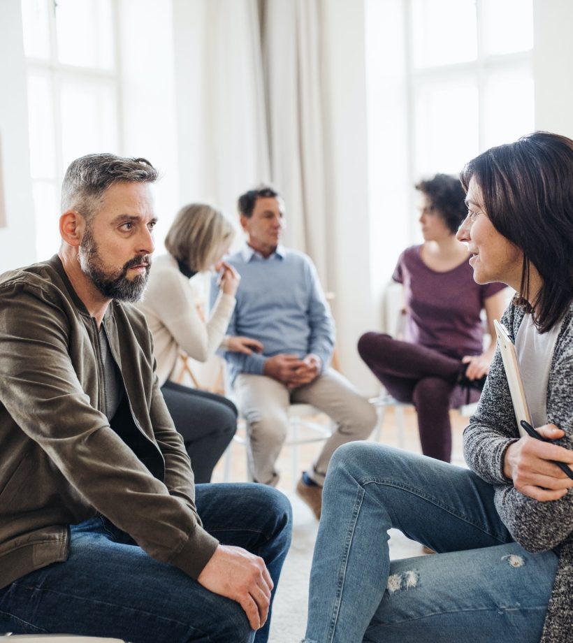 senior-counselor-with-clipboard-talking-to-a-man-during-group-therapy-.jpg senior-counselor-with-clipboard-talking-to-a-man-during-group-therapy-.jpg